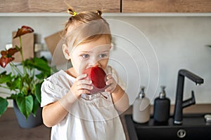 Baby girl blonde eating an apple in the kitchen, concept of healthy food for children