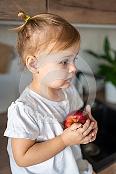 Baby girl blonde eating an apple in the kitchen, concept of healthy food for children