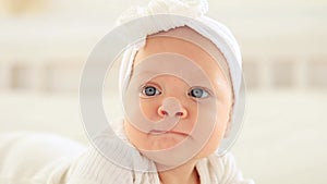 baby girl with blue eyes portrait close-up, happy little baby lying in a bright bedroom in a white bodysuit