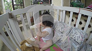 Baby girl bottle-feeding herself in crib