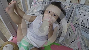 Baby girl bottle-feeding herself in crib