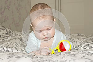 Baby girl boy playing with a rattle on the bed. Little baby looking at a yellow red toy