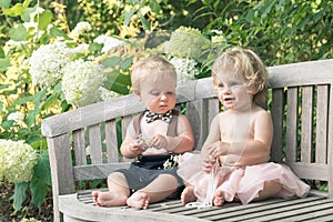 Baby girl and boy sitting on wooden bench and looking on bead