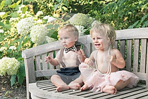 Baby girl and boy sitting on wooden bench and smiling