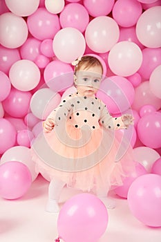 Baby girl celebrate her first birthday. Girl on background of pink balloons