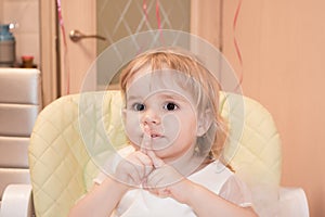 Baby girl celebrates birthday, on a child's chair, shows 2 years with her fingers