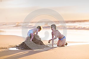 Baby girl climbing sand castle her brother was builded