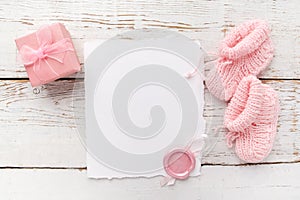 Baby girl clothes, blank card with wax seal and small present box on white wooden background. Flat lay. Owerhad view