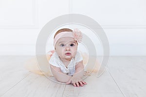 A baby girl is crawling along the floor with an inquisitive and wondering look on her face. Horizontal shot. Cute 6 months girl