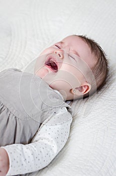 Baby girl crying over white bedcover