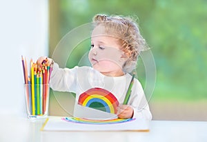 Baby girl with curly hair paiting with colorful pencils