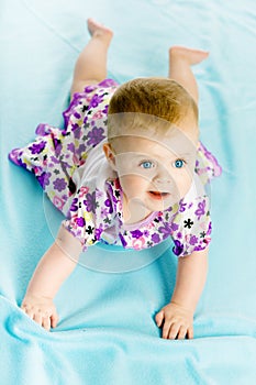 Baby girl in a dress creeps on the blue coverlet