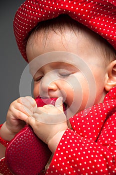Baby girl dressed in a red dress eating a shoe