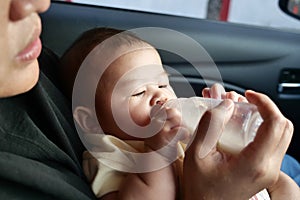 Baby girl drinking formula milk in bottle, mother feed her infant