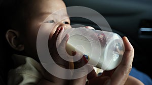 Baby girl drinking formula milk in bottle, mother feed her infant