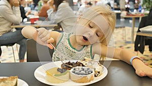 Baby girl eating assorted cakes in a cafe on a blurred background