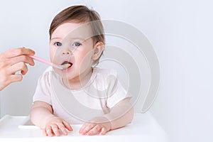 Baby girl eating blend mashed food sitting, on high chair, mother feeding child, hand with spoon for vegetable lunch