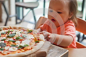 Baby girl eating pizza in italian restaurant, Healthy, unhealthy food, children`s fast food.