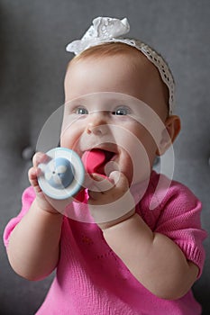 A baby girl european with blond hair bitting a teether toy and happily sincerely smiles. Baby teething concept.