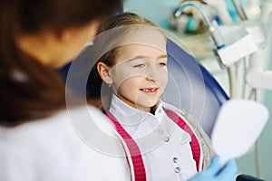 Baby girl examines teeth in a dental mirror