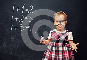 Baby girl in glasses and chalk at a school board with arithmeti