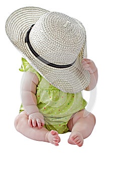 Baby girl in green dress plays peekaboo with big straw hat