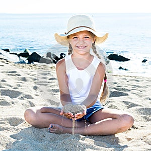 Baby girl in hat playing with sand on sea coast in summer