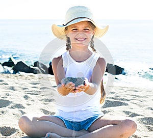 Baby girl in hat playing with sand on sea coast in summer
