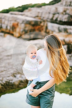 Baby girl in her mother& x27;s arms on a rocky beach