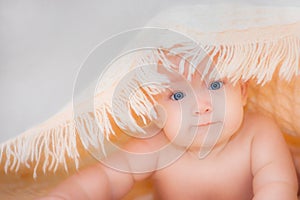 Baby girl is hiding under the coral blanket. Newborn under a blanket on a soft white background. Baby care. Skin care