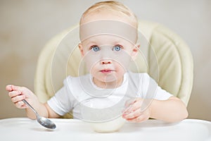 Little girl inquiringly looks at the camera, holding a spoon and about to eat porridge