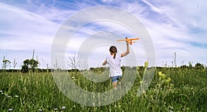 A baby girl is launching a toy airframe glider in a field against a blue sky background with clouds.