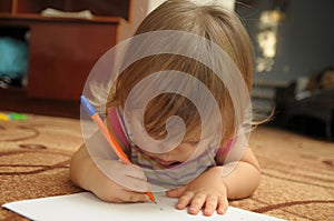 Baby girl learning to write and paint in home environment lying on carpet. Early brain education development concept