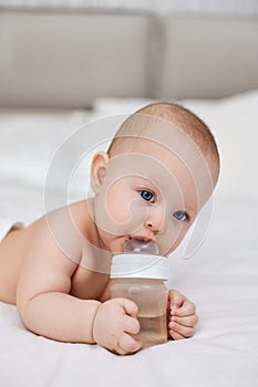 baby girl lies in bed and drinks water from a bottle