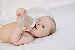 baby girl lies in bed and drinks water from a bottle