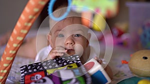 Baby girl lies on her stomach and nibbles on a developmentbook on a development mat, Looking at the camera