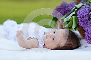 Baby girl with lilac bouquet in basket