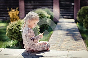 Baby girl with long hair and beautiful dress sits on the doorstep at home and looks at a little doll