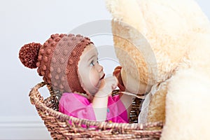 Baby girl looks at face of teddy bear