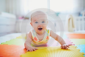 Baby girl lying on colorful play mat on the floor