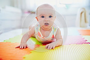 Baby girl lying on colorful play mat on the floor