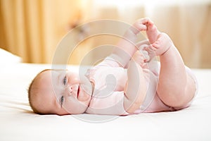 Baby girl lying on white sheet and holding her feet