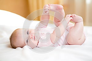 Baby girl lying on white sheet and holding legs