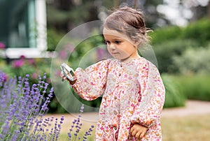 baby girl with magnifier looking at garden flowers