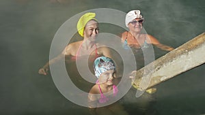 Baby girl, mom and grandmother in a swim in hot saline mineral water bath at a traditional spa outdoor with soft