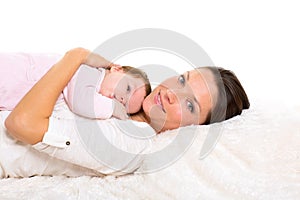 Baby girl and mother lying happy together on white fur