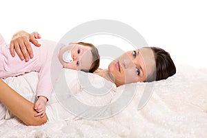 Baby girl and mother lying happy together on white fur