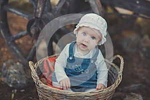 Baby girl with ocean deep blue eyes and pinky cheek wearing white shirt and jeans dress and handmade craft tiny hat sitting in bas photo