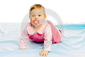 Baby girl with pacifier crawling on the blue coverlet. Studio