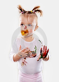 The baby girl with a pacifier in gouache soiled hands and shirt isolated